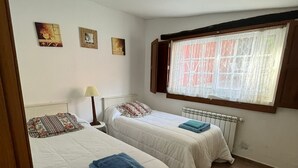 A bedroom with two beds, a radiator, and a window with curtains. - CASA ROMEO housing in typical Galician architecture (Brión)
