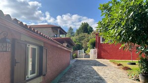 A stone-paved pathway leading to a building with a red wall and a green door. - CASA ROMEO housing in typical Galician architecture (Brión)
