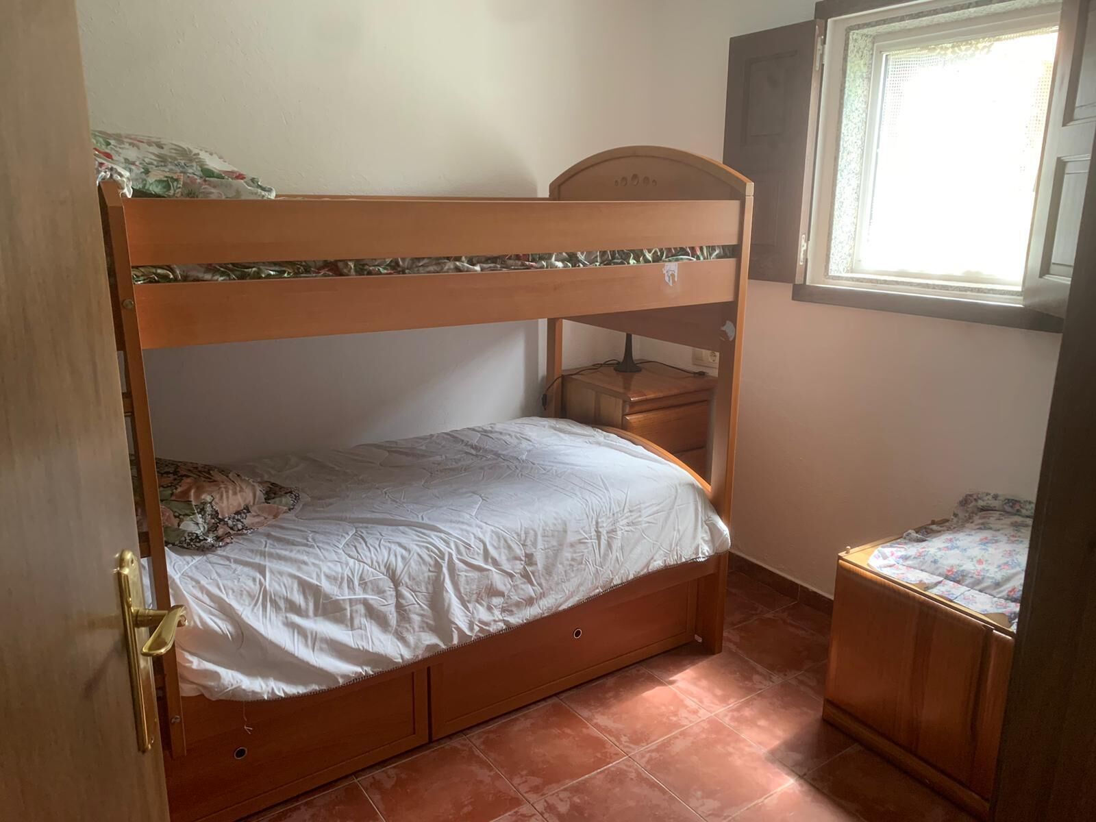 Une chambre avec un lit superposé, une tête de lit en bois, une petite table de chevet et une fenêtre avec des stores.