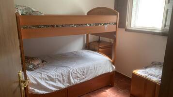 Une chambre avec un lit superposé, une tête de lit en bois, une petite table de chevet et une fenêtre avec des stores.