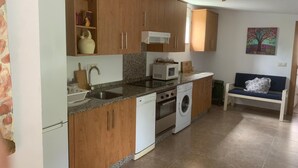 A compact kitchen with wooden cabinets, a microwave, a washing machine, and a sink. - CASA ROMEO housing in typical Galician architecture (Brión)