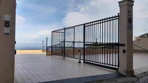 Ein verschlossenes Tor mit Fliesenboden, ein Schild an der Mauer und ein klarer Himmel.