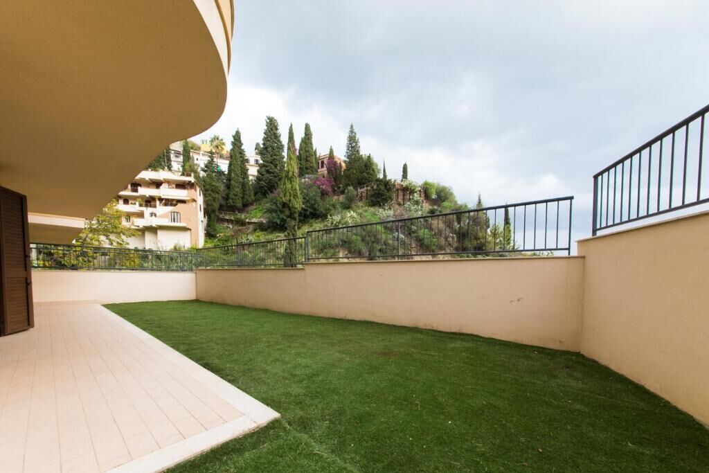 A balcony with a view of a hillside, a grassy area, and a metal railing.