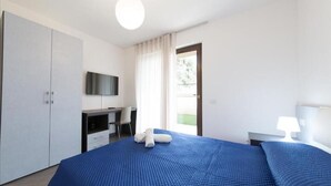 Ein Schlafzimmer mit einem großen Bett, einem Schreibtisch, einem Fernseher und einem Fenster mit Vorhängen.