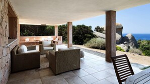 An outdoor patio with wicker furniture, a stone wall, and a view of the sea. - Charming villa with magnificent sea view (Santa Teresa di Gallura)
