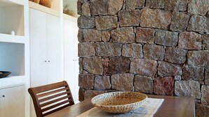 A dining area with a stone wall, wooden table, and chairs. - Charming villa with magnificent sea view (Santa Teresa di Gallura)