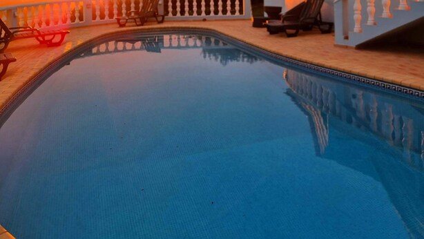 A swimming pool with a view of the sunset, lounge chairs, and a building with a balcony. - Villa with a privileged panoramic view (Loule)