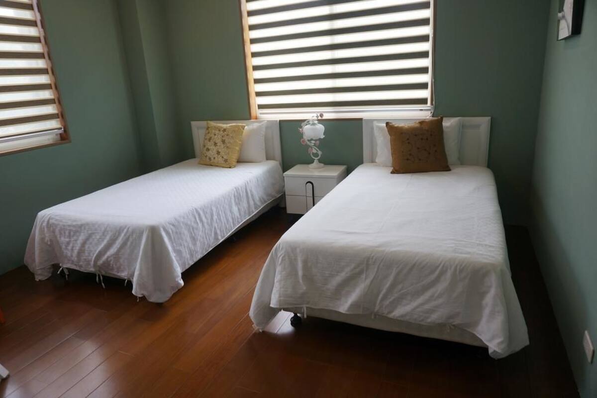 Une chambre avec deux lits simples, une table de chevet et une fenêtre avec des stores.