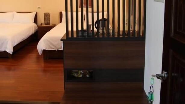 Una habitación de hotel con dos camas, un separador de madera, una mesita pequeña y un cubo de basura.