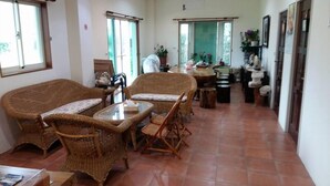 Un amplio salón con mobiliario de mimbre, una mesa de centro de vidrio y piso de baldosas.