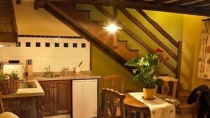 A cozy kitchen with wooden cabinets, a white dishwasher, and a dining area with a table and chairs. - Rural apartment El Mirador de Cazanes for 2 people (Villaviciosa)
