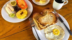 En morgenmadstallerken med ristet brød, et spejlæg og en skål med frugt, herunder papaya, banan og ananas.