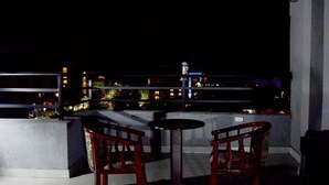 A balcony with two wooden chairs and a small round table, overlooking a cityscape at night. - Flamingo Guest House (Bahir Dar)