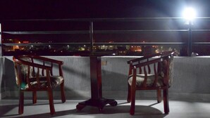 A balcony with two wooden chairs and a table, overlooking a cityscape at night. - Flamingo Guest House (Bahir Dar)