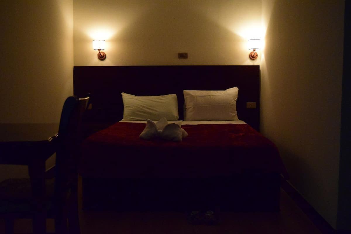 A hotel room with a bed, two bedside lamps, and a chair.
