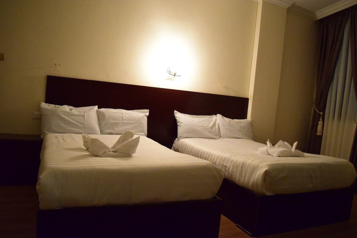 A hotel room with two single beds, each with white linens and pillows, and a nightstand between them.