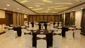 A conference room with multiple tables, white chairs with brown sashes, and ceiling lights. - West Fort Hotel (Bengaluru)
