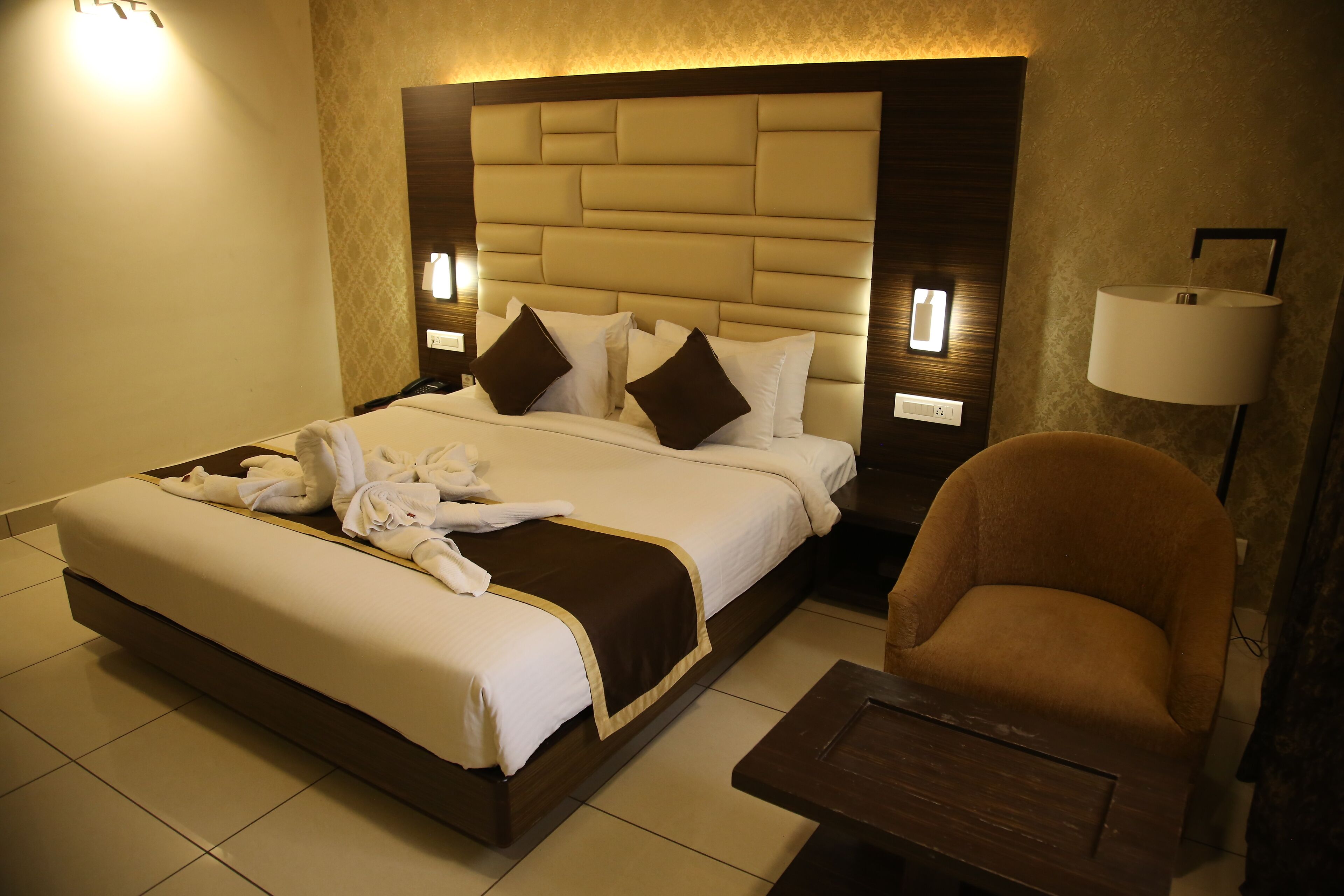 A hotel room with a large bed, a brown armchair, and a small wooden table.