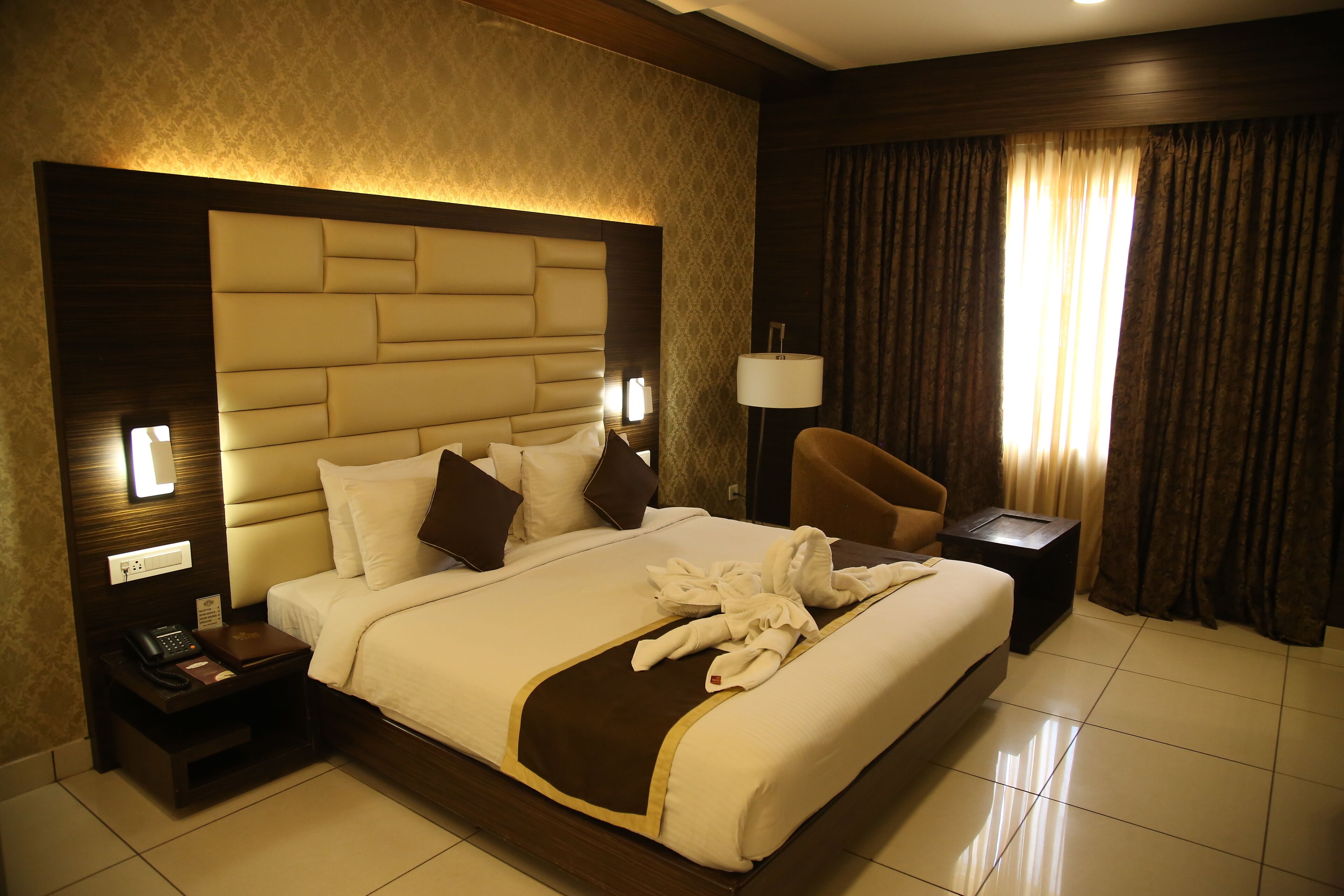 A hotel room with a large bed, a nightstand with a phone, a chair, and a lamp.