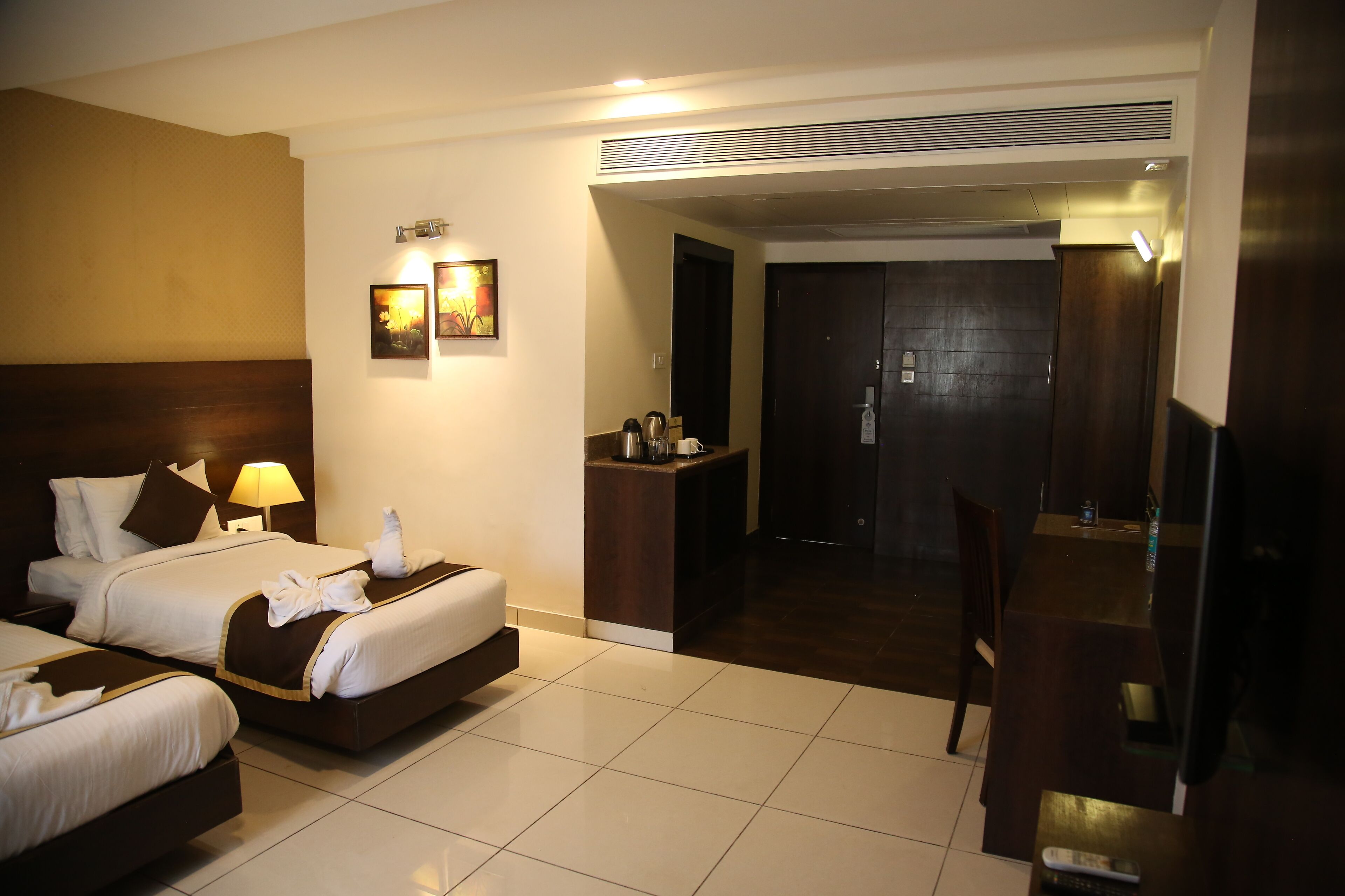 Une chambre d’hôtel avec deux lits, un bureau, une chaise, une petite kitchenette et une porte donnant sur une autre pièce.