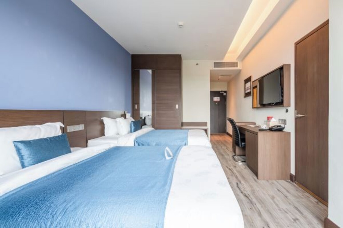 A hotel room with two beds, a desk, a chair, a TV, and a door.