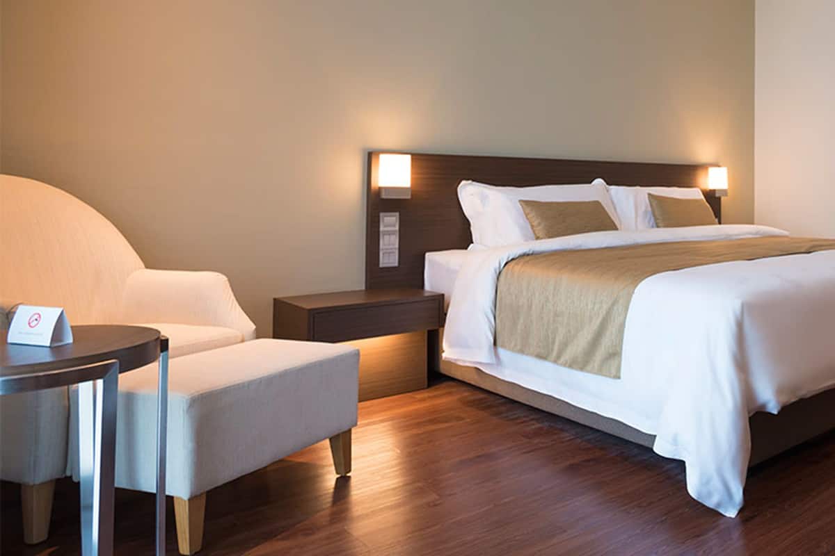 Una habitación de hotel con cama, mesita de noche, silla y una mesita con lámpara.