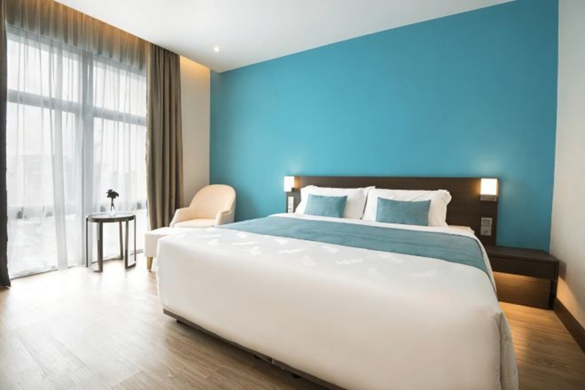 A hotel room with a large bed, a nightstand, a chair, and a small table.