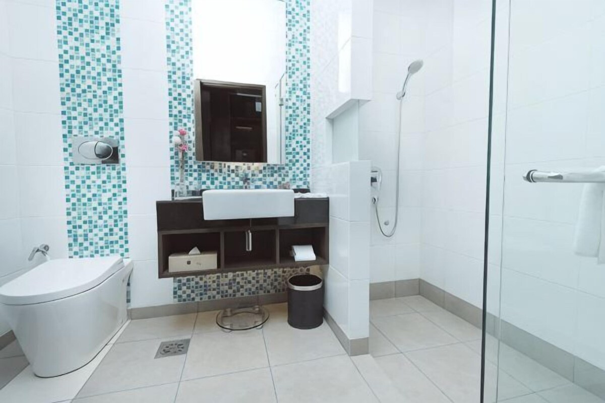 A bathroom with a toilet, sink, mirror, shower, and tiled walls.