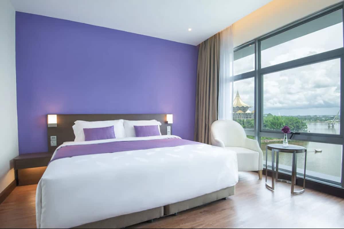 Habitación de hotel con una cama grande, vista a un puente y un paisaje urbano.
