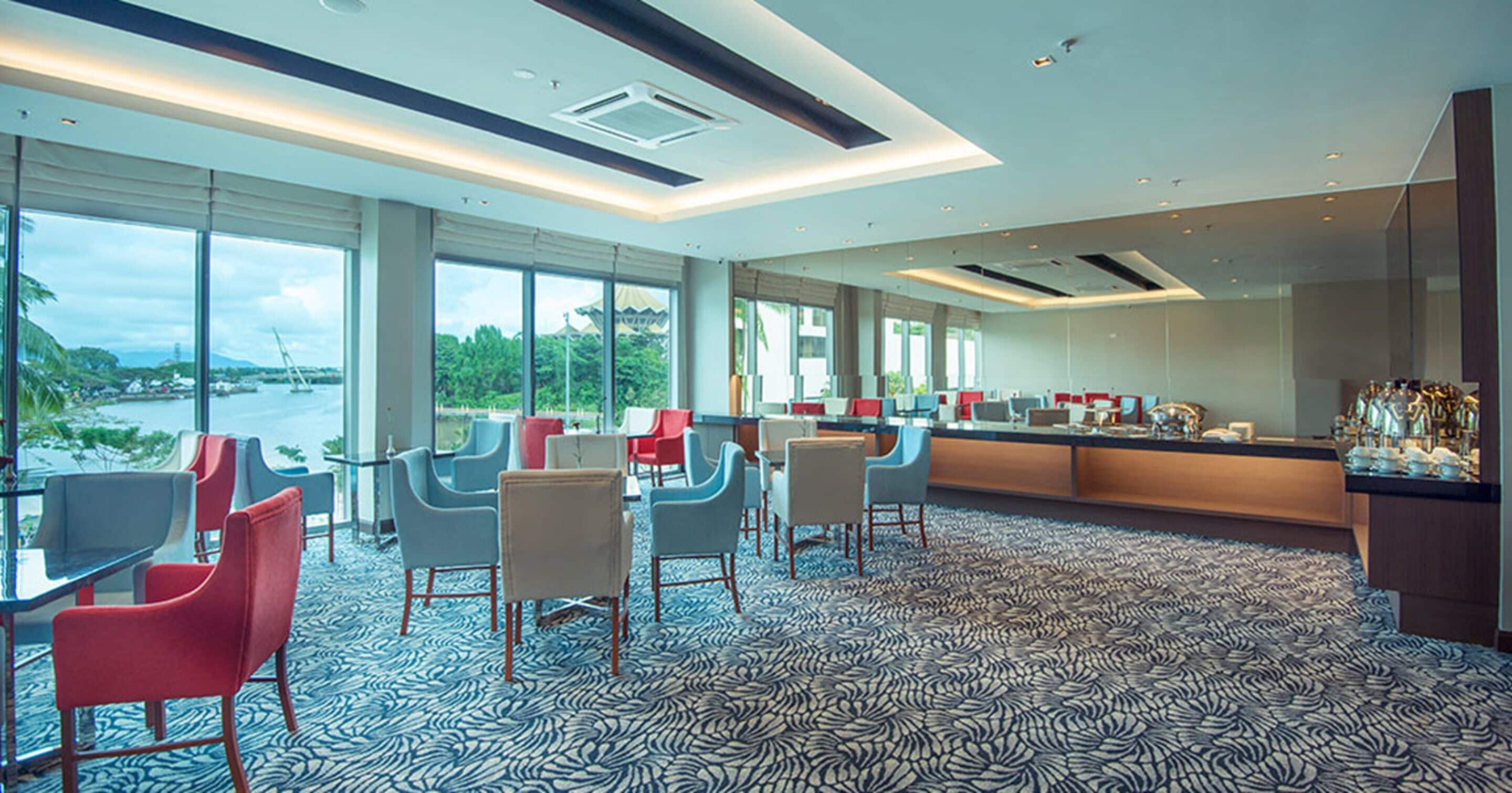 A modern hotel lobby with a large seating area, a reception desk, and large windows offering a view of the outdoors.