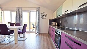 A modern kitchen with stainless steel appliances, a dining area with purple chairs, and a large window with curtains. - Apartment for up to 7 people with views to the mountains and the sea (Starigrad)