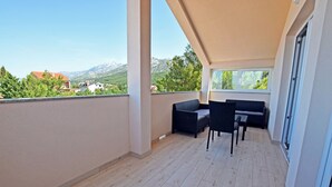 A balcony with a sofa and table, wooden flooring, and a view of mountains and houses. - Apartment for up to 7 people with views to the mountains and the sea (Starigrad)