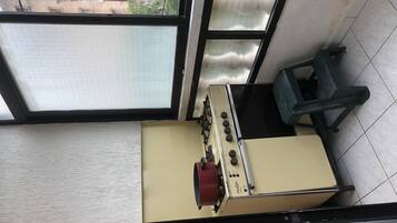 A compact kitchen with a gas stove, a small stool, and a window overlooking a building.