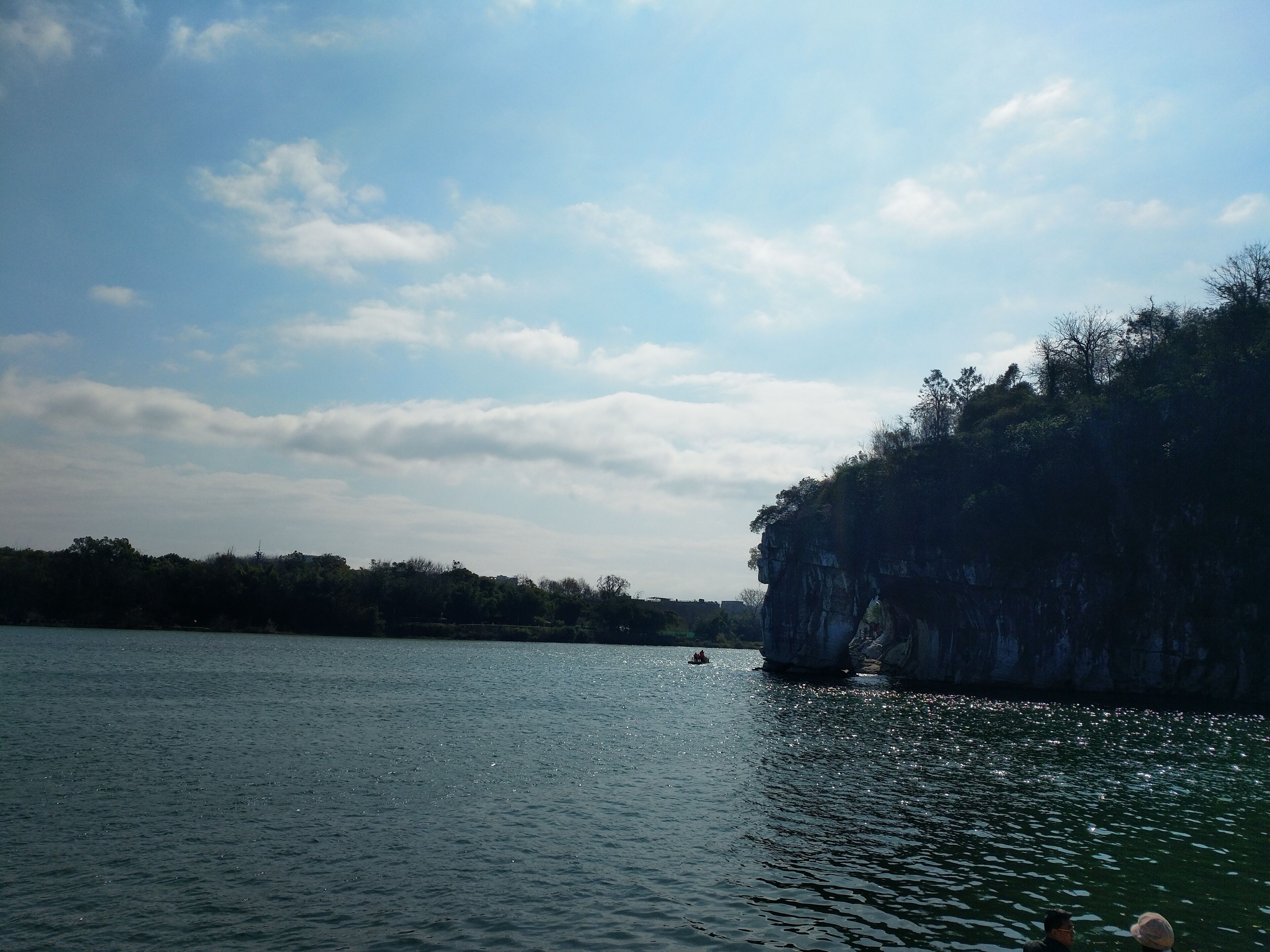 A calm river with a rocky cliff on one side and a boat in the distance.