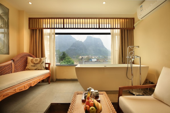 Una habitación con sofá, una mesa con fruta, una bañera y vistas a la montaña.
