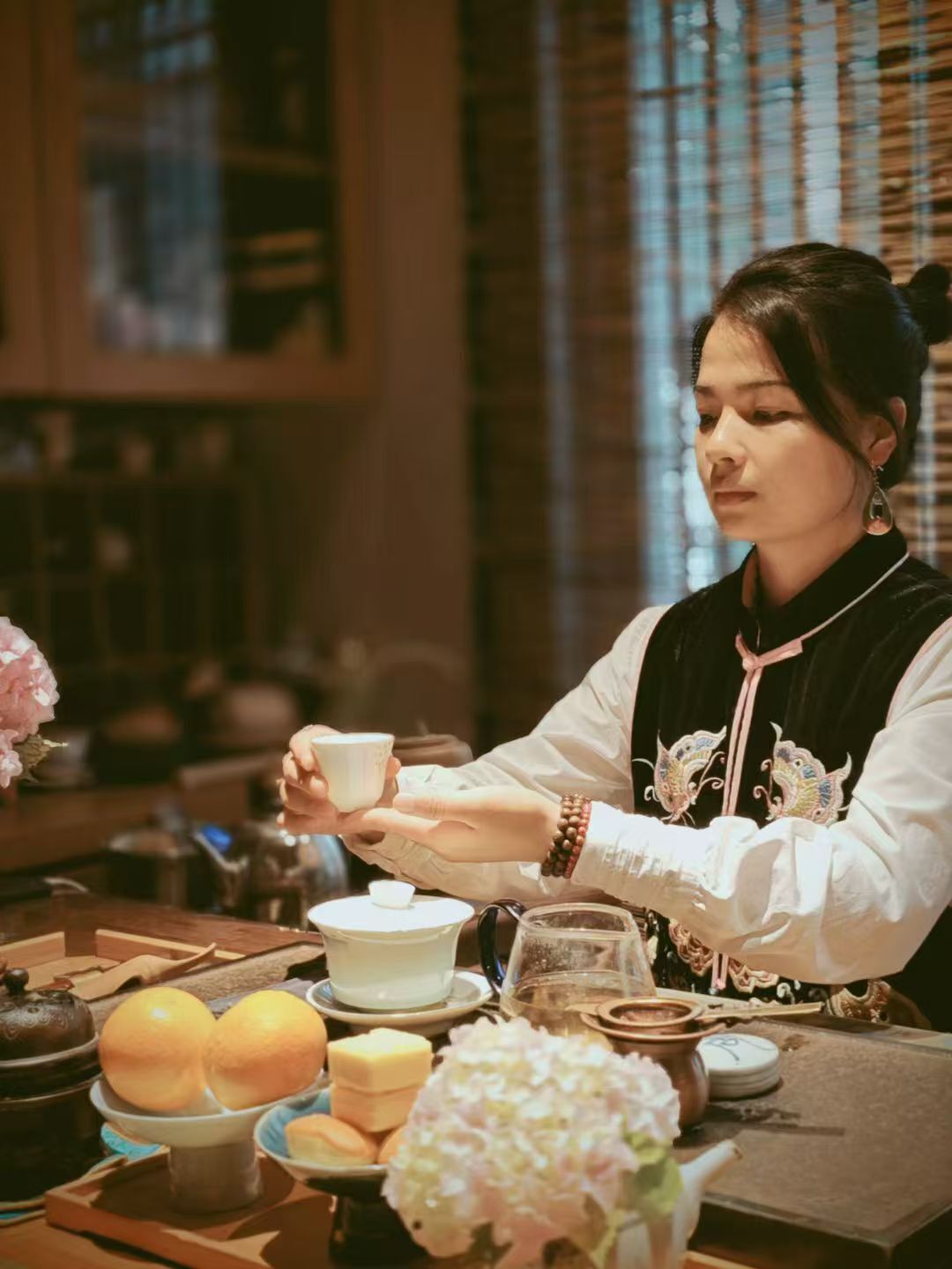A person seated at a table with various items including a teapot, cups, and food.
