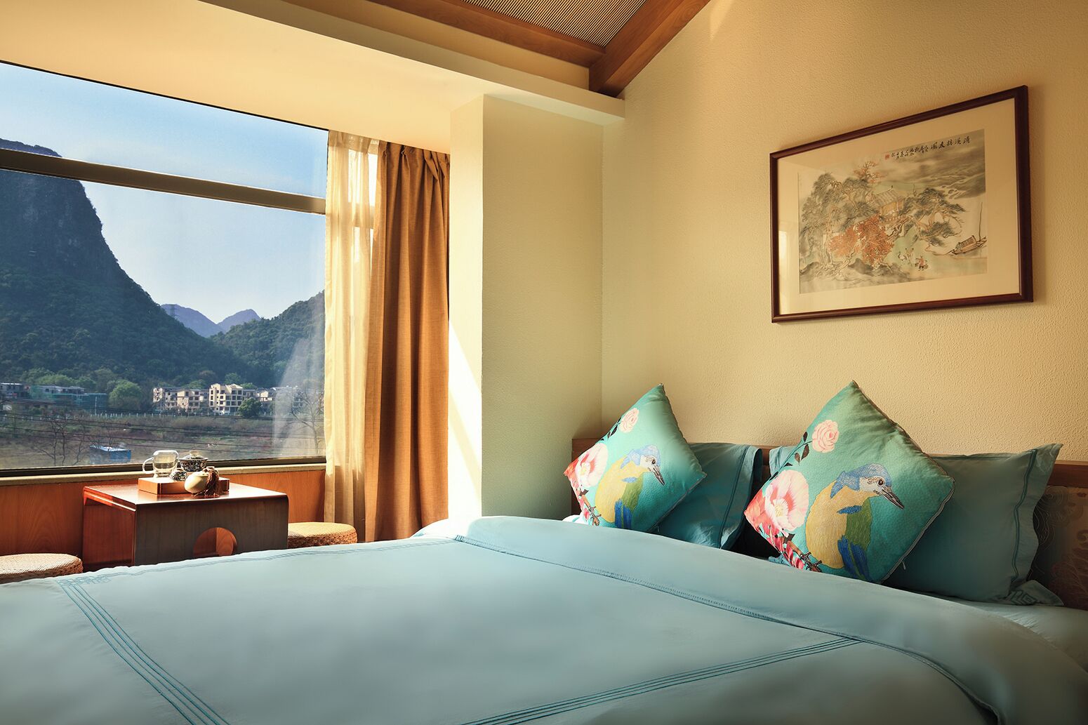 A bedroom with a large bed, a nightstand, a window with curtains, and a framed picture on the wall.