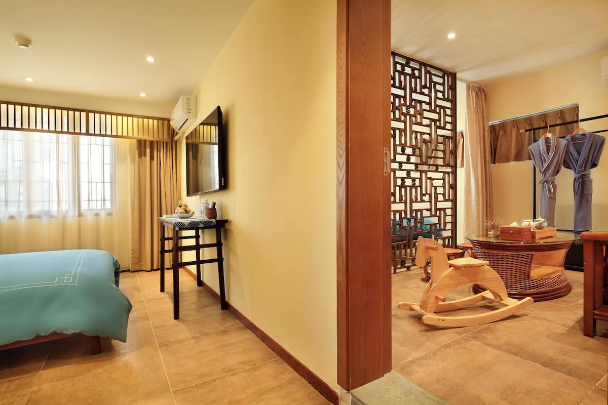 A hotel room with a bed, a desk, a rocking chair, a TV, and a bathroom with towels and a shower curtain.