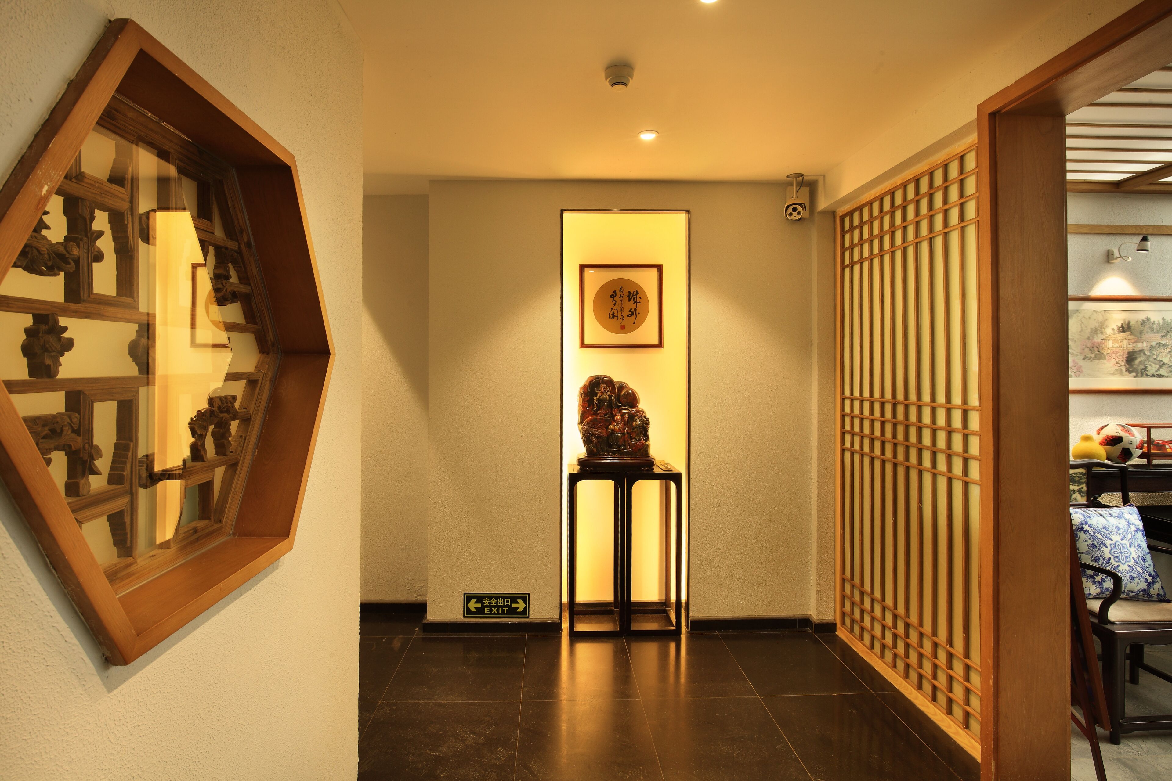 A hallway with a traditional Japanese-style sliding door, a framed artwork on a stand, and an exit sign.