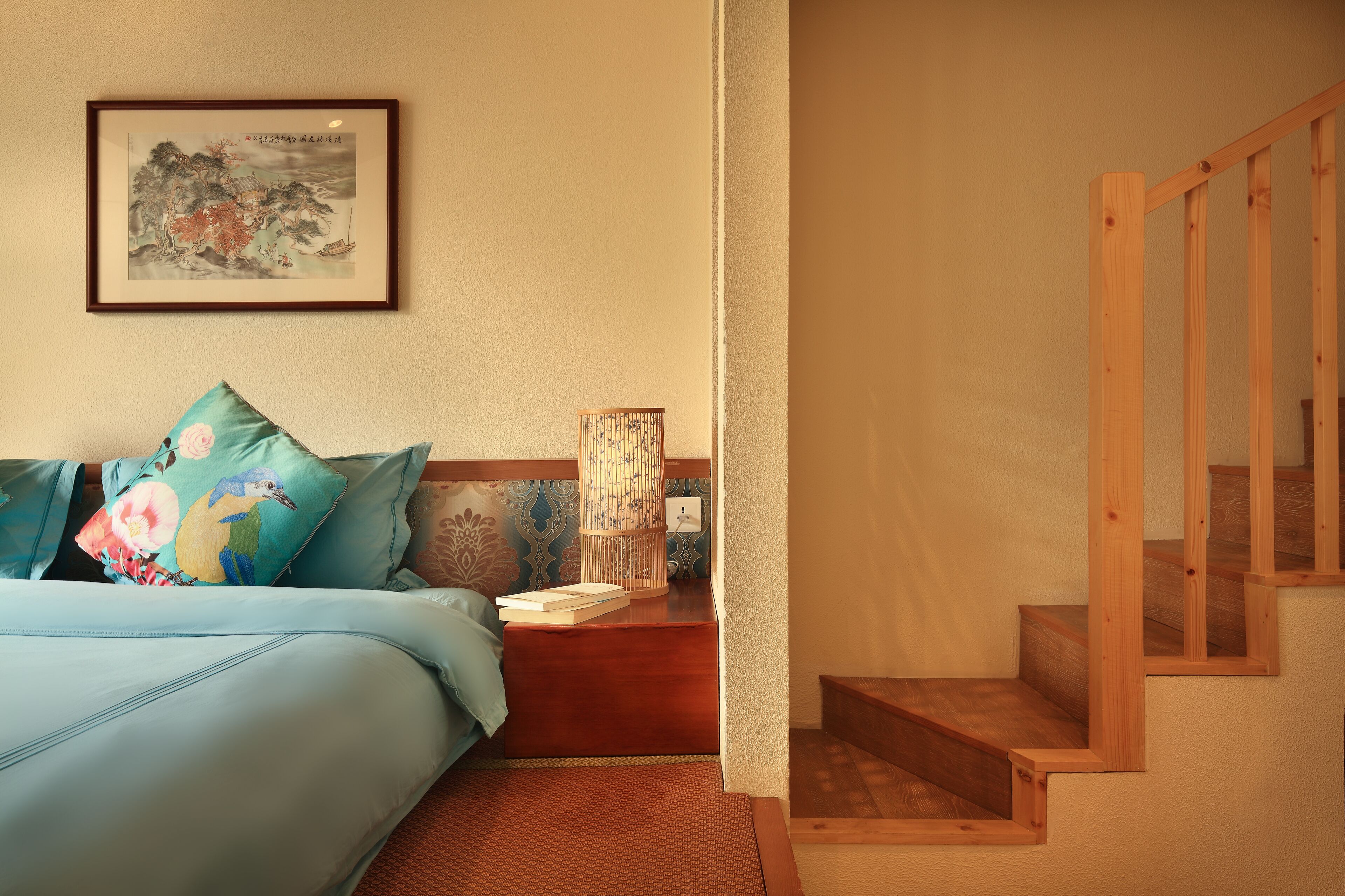 A bedroom with a bed, pillows, a nightstand, a lamp, and a wooden staircase.