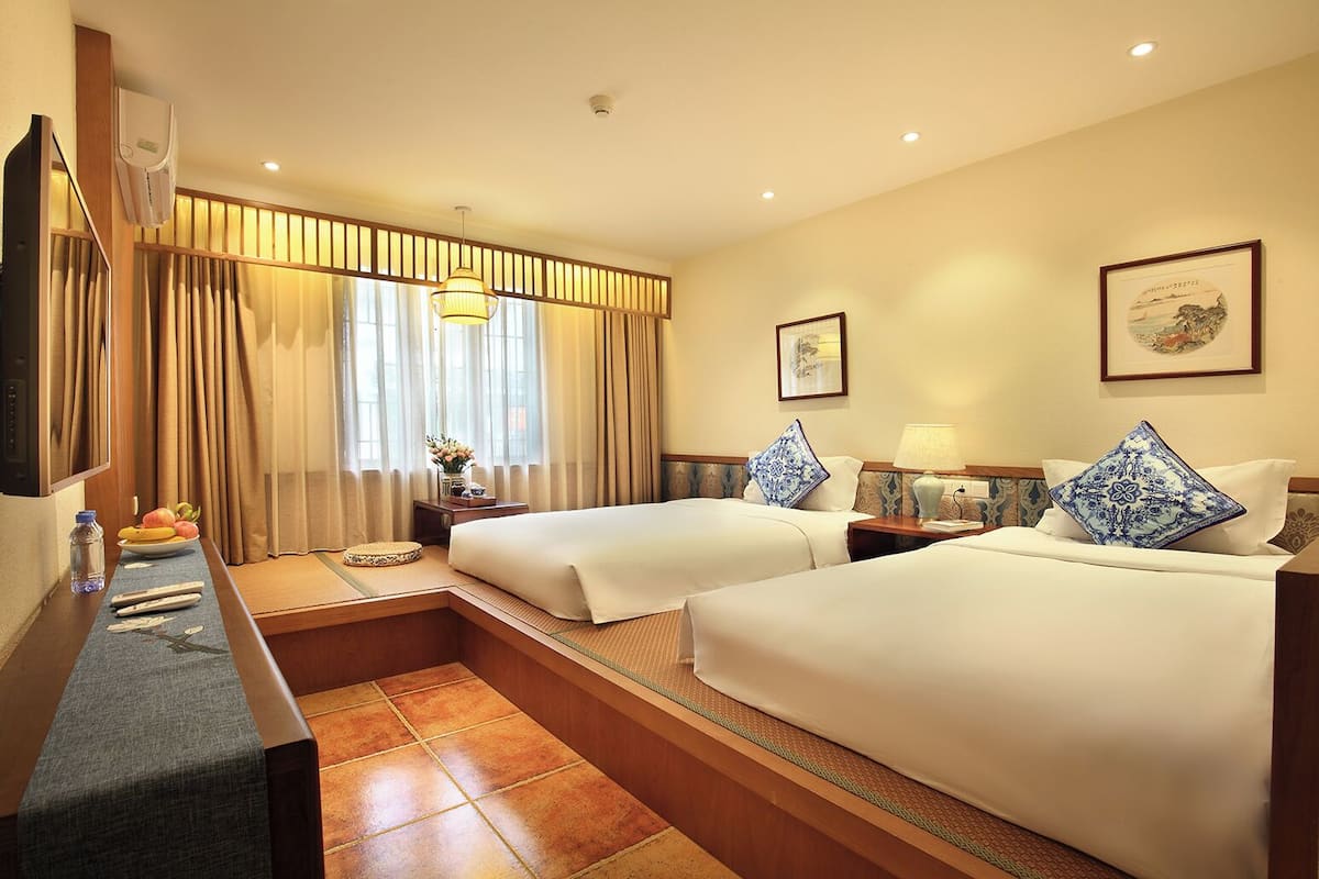 A hotel room with two beds, a desk with a chair, a TV, and a window with curtains.