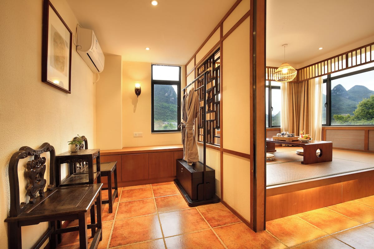 A traditional Japanese room with tatami flooring, a sliding door, a view of mountains, and a dining area with a low table and chairs.