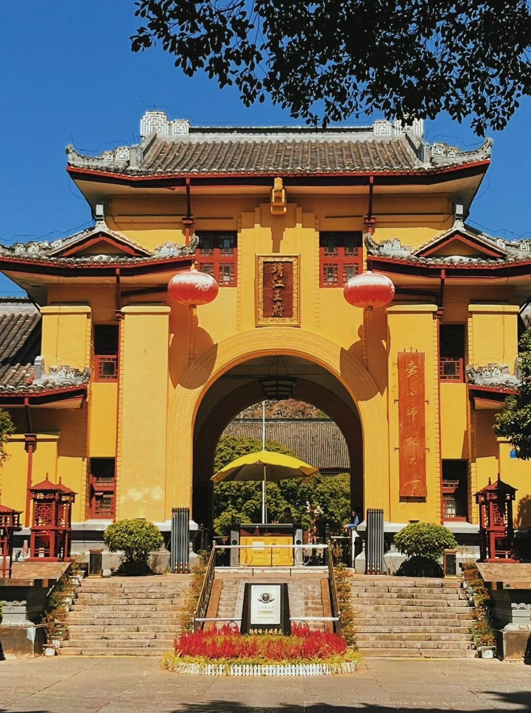 Une porte chinoise traditionnelle à la façade jaune, ornée de lanternes rouges et dotée d’une arche centrale.