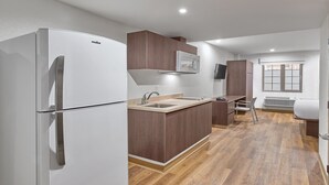 A compact kitchen with a white refrigerator, wooden cabinets, a built-in microwave, and a window with a view.