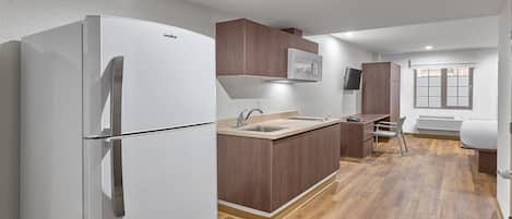A compact kitchen with a white refrigerator, wooden cabinets, a built-in microwave, and a window with a view.