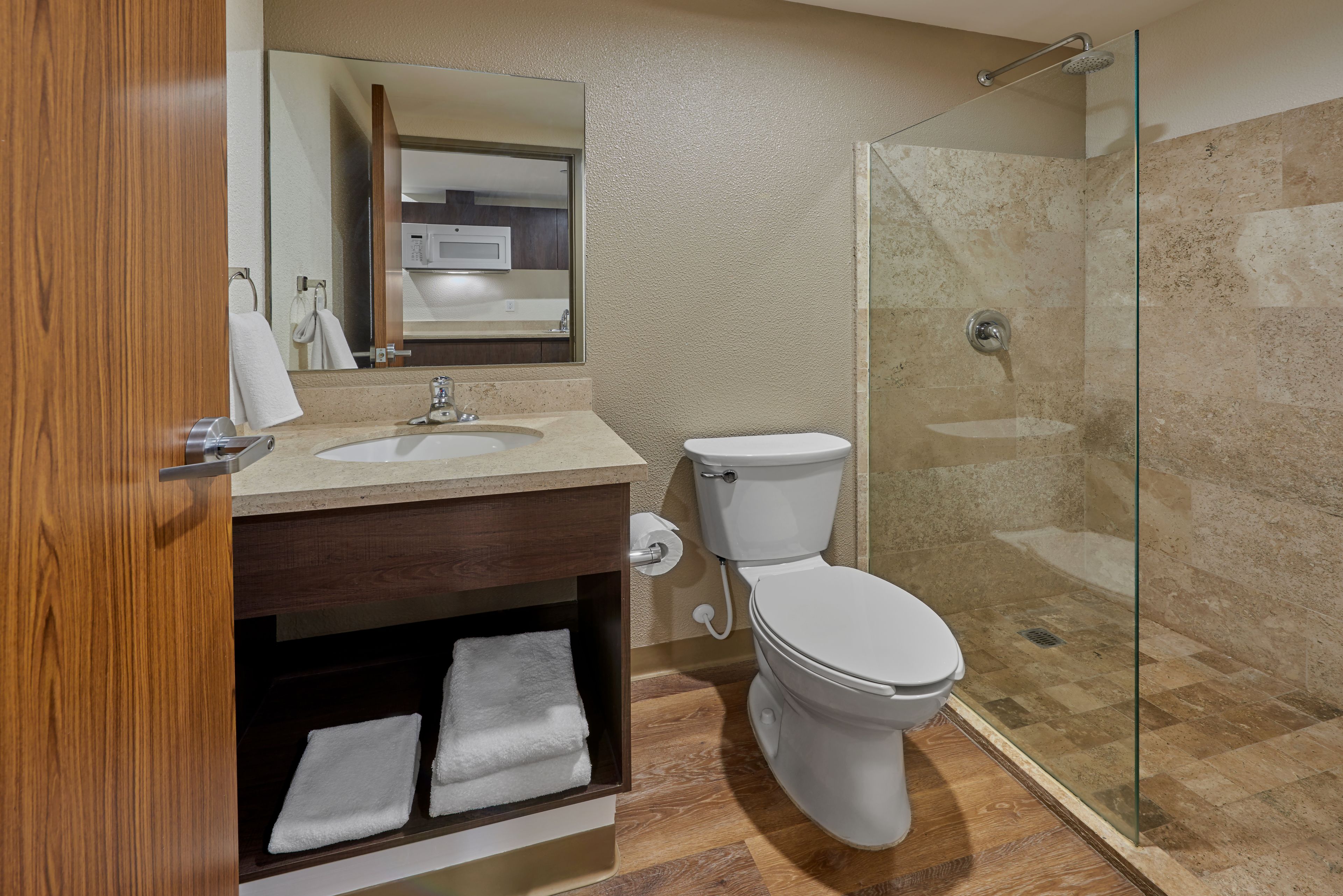 A modern bathroom with a wooden vanity, a white toilet, and a glass-enclosed shower area.