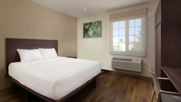 A hotel room with a bed, a desk, a window with a view, and a painting on the wall.