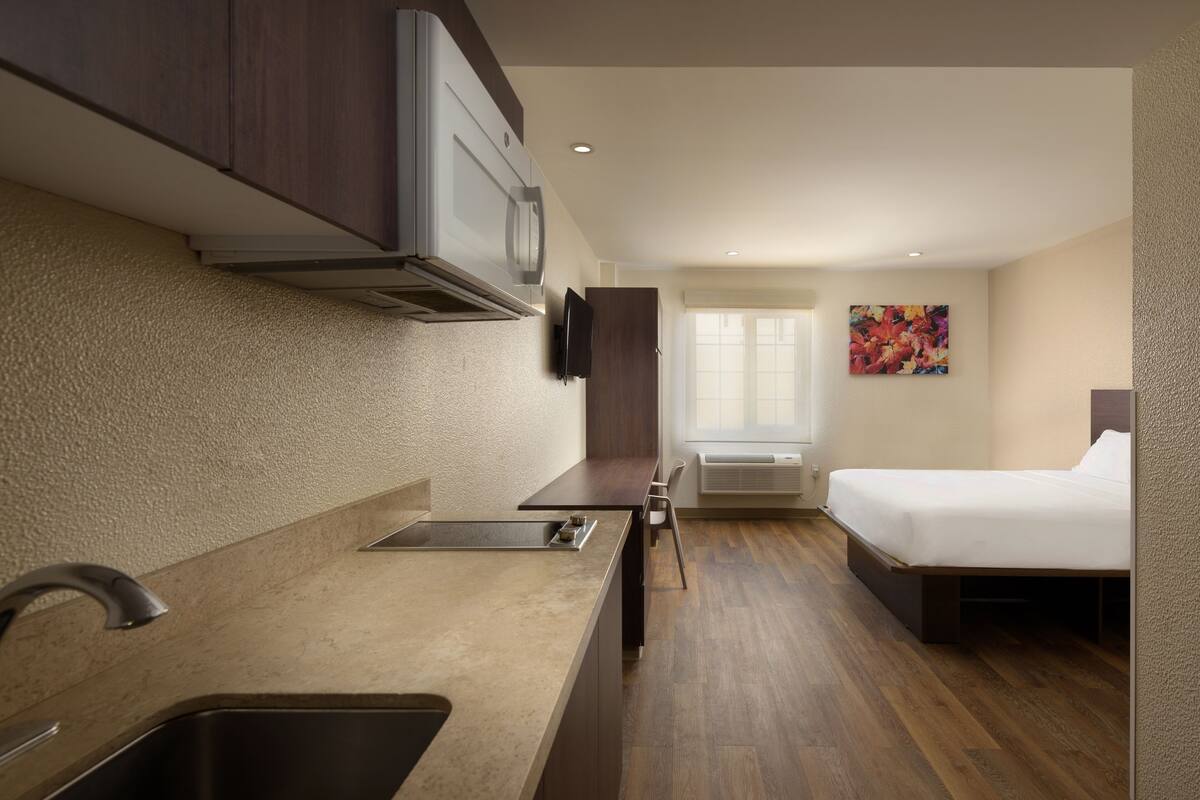 A compact hotel room with a kitchenette, a bed, and a window.