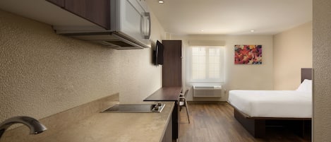 A compact hotel room with a kitchenette, a bed, and a window.
