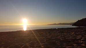 Ein Strand mit felsigem Ufer und freiem Blick auf den Sonnenuntergang über dem Wasser.